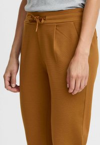 Bruna sweatpants med dragsko i midjan, texturerat tyg, sidfickor och en smal bendesign. Synliga sömdetaljer.