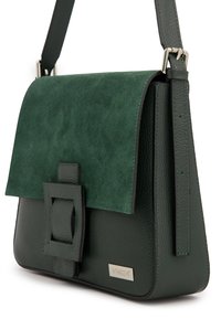 Grüne Ledertasche mit Wildlederklappe, strukturiertem Finish, rechteckiger Form und dekorativer Schnalle. Markenschild sichtbar.