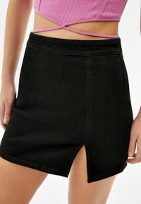 Černá denimová mini sukně s předním rozparkem, čistými liniemi a přiléhavým střihem. Materiál má hladkou texturu a minimální švy.