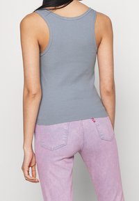 Grå ribbad linne med en åtsittande design. Baksidan har breda axelremmar och en fåll som svänger svagt, kombinerad med rosa jeans.