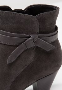 Bottine en daim gris foncé avec un petit talon empilé et un nœud en cuir décoratif sur le côté.