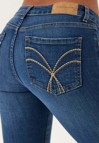 Blå denimjeans med ett dekorativt sömnadsmönster på bakfickorna. Märket är i beige. Har en kroppsnäv design och lätt stretch.