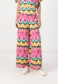 Pantaloni a gamba larga caratterizzati da un vivace design a fantasia con tonalità di rosa, verde, giallo e nero, realizzati in un tessuto leggero.