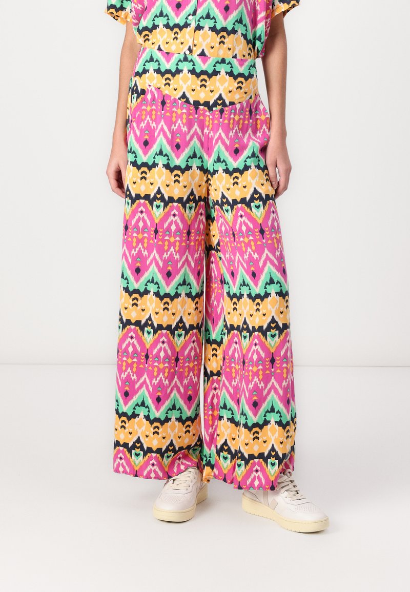 Pantaloni a gamba larga caratterizzati da un vivace design a fantasia con tonalità di rosa, verde, giallo e nero, realizzati in un tessuto leggero.