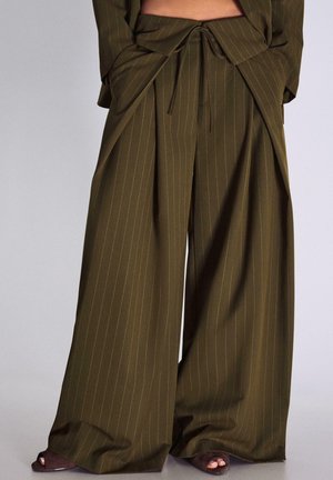Pantalon large olive à fines rayures avec taille à cordon, associé à des talons ouverts foncés.