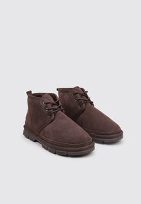 Botines de ante marrón con punta redondeada, diseño con cordones y superficie texturizada. Suela de goma duradera con surcos para tracción.