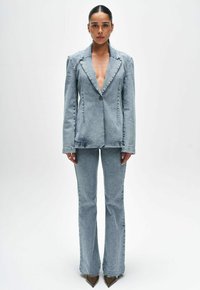 Jeansowy garnitur w jasnym niebieskim odcieniu; dopasowana marynarka z klapami typu notch i jednym guzikiem, w połączeniu z spodniami dzwonami. Gładka faktura, minimalne detale.