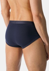 Tumman laivaston siniset puuvillabriiffit, joissa on sileä pinta ja tiukka istuvuus. Ominaisuuksiin kuuluu erottuva vyötärö ja minimaalinen sauman yksityiskohta lahkeissa.