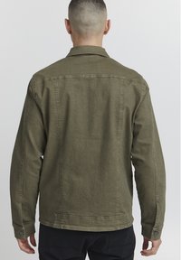 Oljčno zelena denim jakna s ravnim krojem, z gumbnimi manšetami in vidnimi šivi. Zadnji pogled prikazuje čisto obdelavo in minimalne podrobnosti.