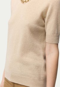 Ljusbeige kortärmad stickad tröja i mjukt material, med ribbad fåll och muddar, samt en slät textur och minimalistisk design.