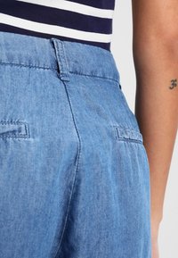 Světle modré denimové kalhoty s hladkým povrchem, vybavené páskem, zadními kapsami a jemnými švy.