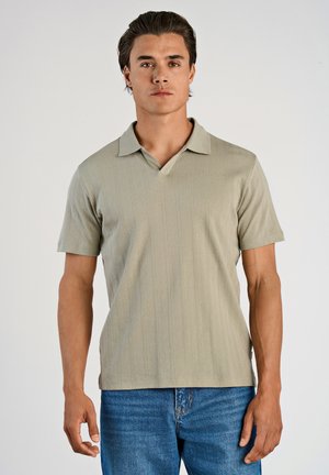 Light green polo shirt with a V-neck, short sleeves, a textured vertical pattern, and a flat collar, paired with blue denim jeans.