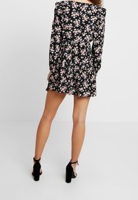 Černé květinové šaty s dlouhými rukávy, volánkovými ramenními částmi a přiléhavým pasem, s růžovými a modrými květy na tmavém pozadí.