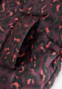 Gewatteerd jack met een bordeauxrode achtergrond en zwarte en koraalkleurige luipaardprint. Voorzien van oranje accenten in contrastkleur en versterkte stiksels.