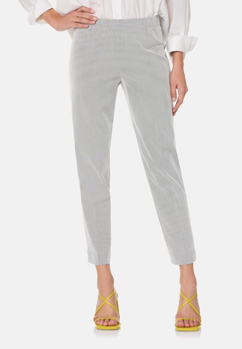 Pantalon rayé gris et blanc avec une coupe ajustée, jambes effilées et taille élastique. Porté avec des sandales à lanières jaunes.
