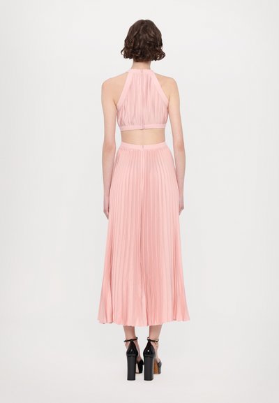 Pleated pink two-piece outfit featuring a cropped halter top and long skirt. The skirt has a flowing design, complemented by black high heels.