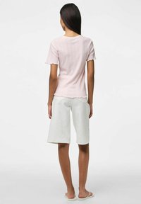 Jasnoróżowa bluzka z krótkim rękawem o teksturowanym wzorze i falbaniastych krawędziach, w połączeniu z białymi szortami do kolan i jasnymi sandałami.