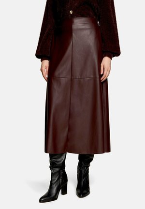 Femme portant une jupe midi en simili cuir marron foncé, des bottines noires à talons et un haut à manches longues marron duveteux avec un bouton doré.