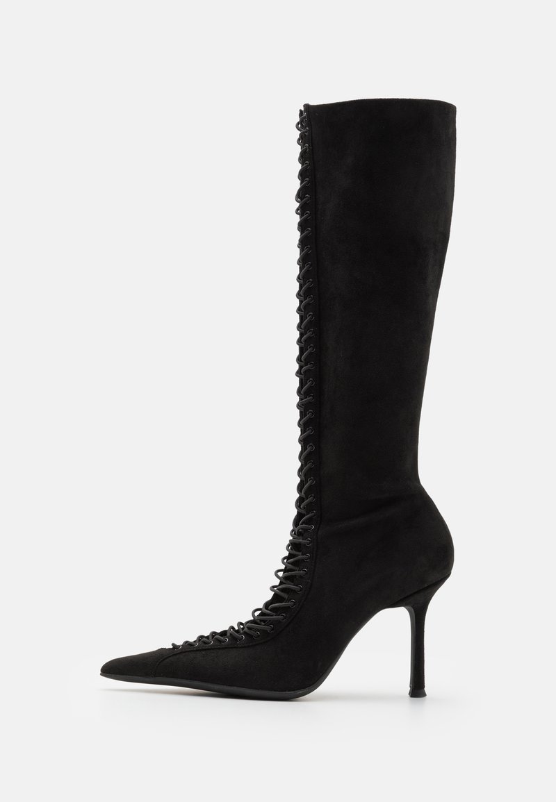 Boot cu toc înalt, din suede negru, de lungime până la genunchi, cu vârf ascuțit, având detalii din dantelă pe lateral și o siluetă elegantă.