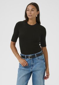 Zwart, kort mouw, aansluitend top gemaakt van ribbelstof, gecombineerd met hooggeknoopte blauwe jeans en een zwarte riem. Minimalistisch ontwerp met een ronde halslijn.