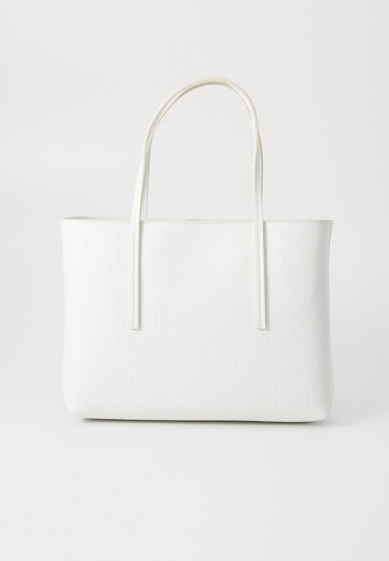 Tote bag bianca con un sottile motivo geometrico a diamante e doppi manici, su uno sfondo leggero e semplice.