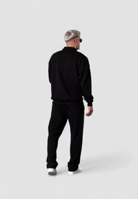 Schwarzes Sweatshirt- und Hosen-Outfit aus weichem Stoff mit lässiger Passform. Die Person steht mit dem Rücken zur Kamera und trägt Sonnenbrillen.