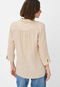 Beige linen shirt with a pointed collar, three-quarter sleeves with slits, and a gathered back detail, worn over blue jeans.