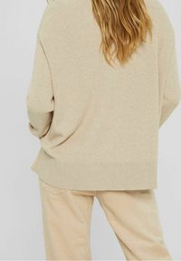 Beige gebreide trui met ribbeltextuur, relaxte pasvorm en een iets verlengde achterkant. Gecombineerd met lichtbeige ribfluwelen broek.