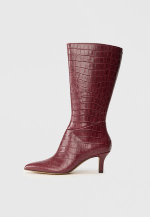 Magas burgundi színű bokacsizma krokodilbőr textúrával, hegyes orral és kislábúval semleges háttér előtt.