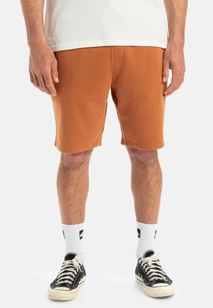 Orange cotton shorts with a relaxed fit, featuring stitched seams and an elastic waistband, paired with white socks and black sneakers.