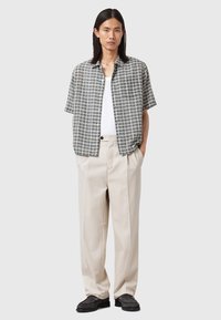 Short-sleeve, checkered shirt in gray and white, paired with cream-colored, pleated trousers and black shoes. Simple button closure.