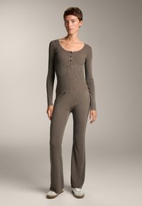 Barna bordázott kötött hosszú ujjú felső gombos részletekkel, hozzá illő, testhezálló, flared nadrággal párosítva. Az anyaga texturált és puha, laza szabású.