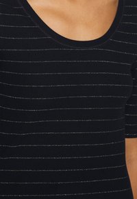 Černý top s krátkým rukávem a kulatým výstřihem, zdobený vodorovnými stříbrnými metalickými pruhy na žebrované textuře.