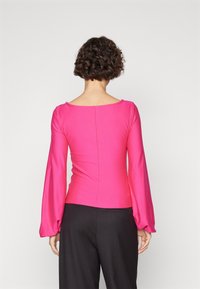 Tight pink långärmad topp med fyrkantig halsringning och något puffade ärmar, med en sömdetalj på baksidan. Blandmaterial av bomull.