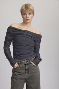 Svakert, gjennomsiktig, mørkegrå topp som går av skuldrene, laget av teksturert stoff, kombinert med høyt liv, gråmelerte jeans. Lange, sammenkrøllede ermer.
