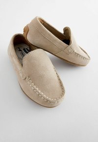 Mocassins en daim beige à enfiler avec des accents cousus et une semelle en caoutchouc flexible. Le design présente une texture lisse et une forme de nez arrondi.
