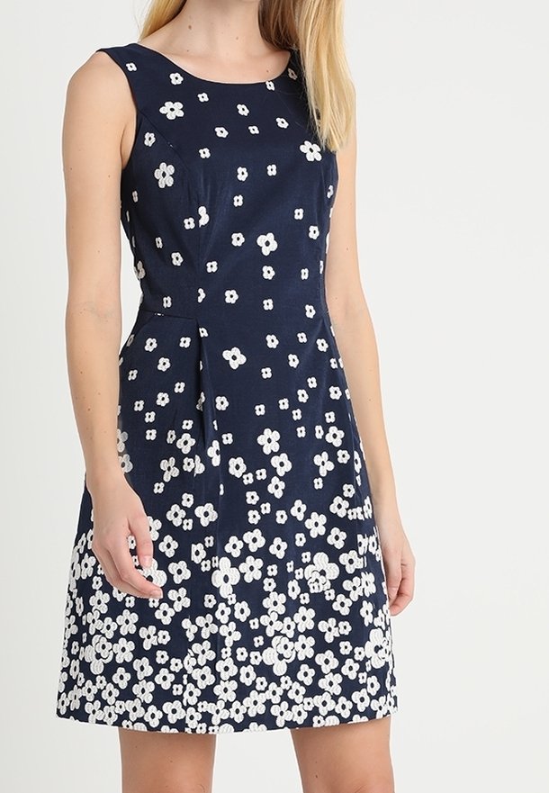 Femme portant une robe bleu marine sans manches avec un motif floral blanc concentré davantage autour de la jupe.