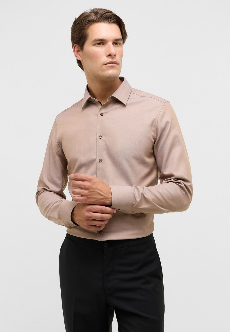 Camicia button-up marrone chiaro con una texture liscia, maniche lunghe e un colletto classico, abbinata a pantaloni neri.