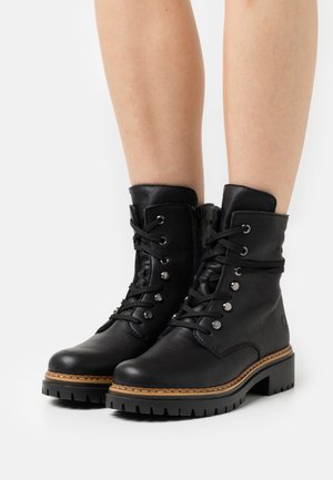 Schwarze Leder-Ankle-Boots mit runder Zehenform, metallenen Ösen und Schnürung. Mit einem seitlichen Reißverschluss und einer strukturierten Sohle mit gestapeltem Absatz.