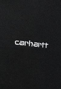 Μαύρο ύφασμα με ριγωτή υφή διαθέτει κεντητό λογότυπο "carhartt" σε λευκό χρώμα, τοποθετημένο κεντρικά για καλύτερη ορατότητα.