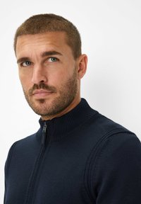 Maglione zip-up navy con colletto alto, motivo a maglia testurizzata e dettagli a coste lungo il collo e le spalle.