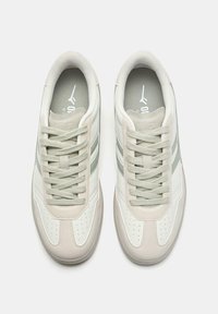 Białe i jasnoszare sneakersy z gładkiej skóry, z perforowanym noskiem, dwoma jasnooliwkowymi paskami i teksturowanymi sznurowadłami. Klasyczny sportowy design.