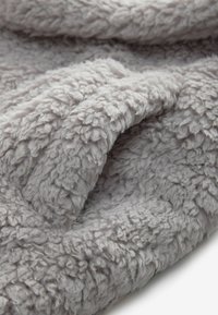 Lys grå fleece tæppe med en blød, tekstureret overflade og et bølget, fluffy mønster. Stoffet falder glat og ser hyggeligt ud.