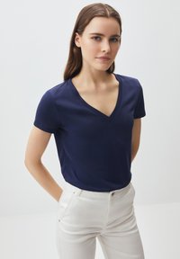 T-shirt blu navy con scollo a V realizzato in tessuto morbido, con maniche corte e design attillato. Abbinato a pantaloni su misura di colore chiaro.