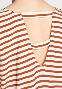 Acercamiento al escote trasero de una blusa a rayas marrón y blanca con un corte en V y un detalle de tira horizontal a través de la abertura.