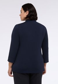 Top blu navy a maniche lunghe con colletto in pizzo texturizzato e maniche aderenti con un delicato dettaglio arrotolato ai polsini.