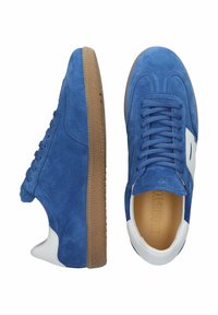 Mėlyni zomšiniai sportbačiai su baltais akcentais, plokščiomis raišteliais, guminiais padais ir tekstūruota protektoriaus danga, turi apvalią noselę ir mažos viršutinės dalies dizainą.