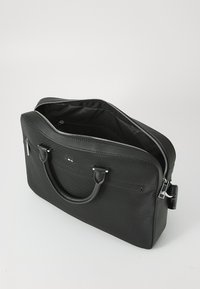 Borsa a tote nera con texture, manici doppi, chiusura con zip e tasca interna. Presenta un design minimalista con dettagli hardware sottili.