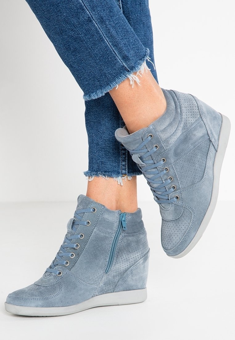Gray suede wedge sneakers with a zipper detail, textured surface, round toe, and perforated accents, paired with cropped denim jeans.