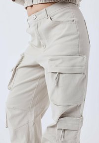 Pantalones cargo beige hechos de algodón, con múltiples bolsillos laterales, cierre de botón y una tela texturizada y transpirable.